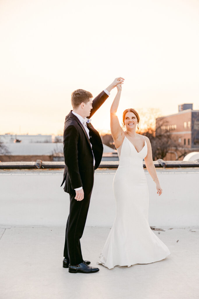 The groom twirls the bride on the venue rooftop. The Chicago sun sets behind them. 