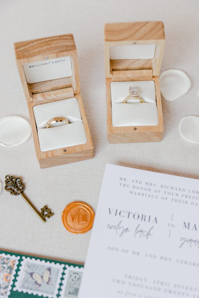 A view from above showing a wedding detail. Two ring boxes are in focus holding the diamond and gold wedding band. 